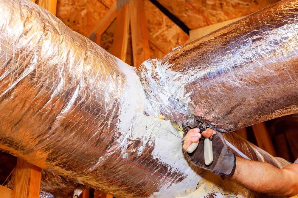 Gloved hands sealing a duct pipe joint