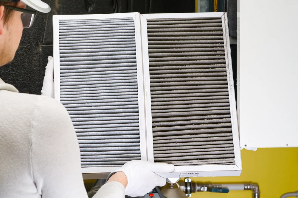 Technician holding a clean HVAC air filter and a dirty one side by side.