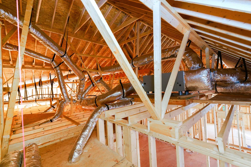 Attic with exposed wooden beams and shiny metal HVAC ducts running through, showcasing heating and cooling infrastructure.