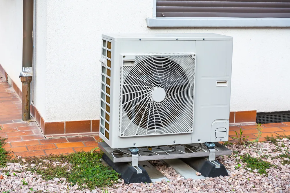Outdoor air conditioning unit on a gravel surface next to a building wall.