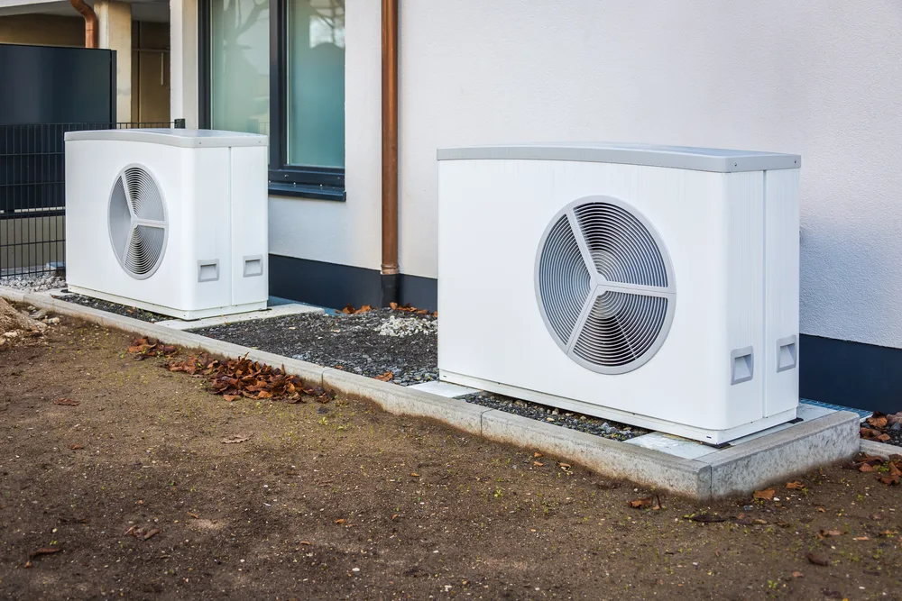 Two white outdoor HVAC units beside a building on concrete slabs.