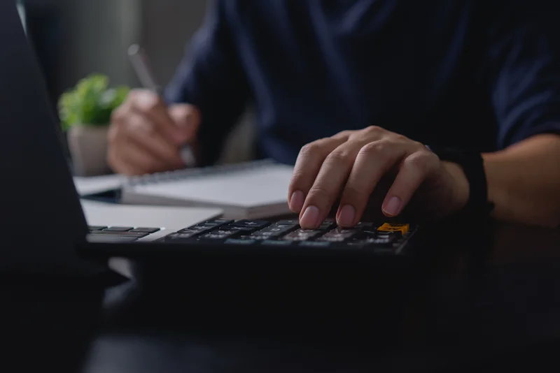 Person typing on a calculator with a pen and notebook nearby.