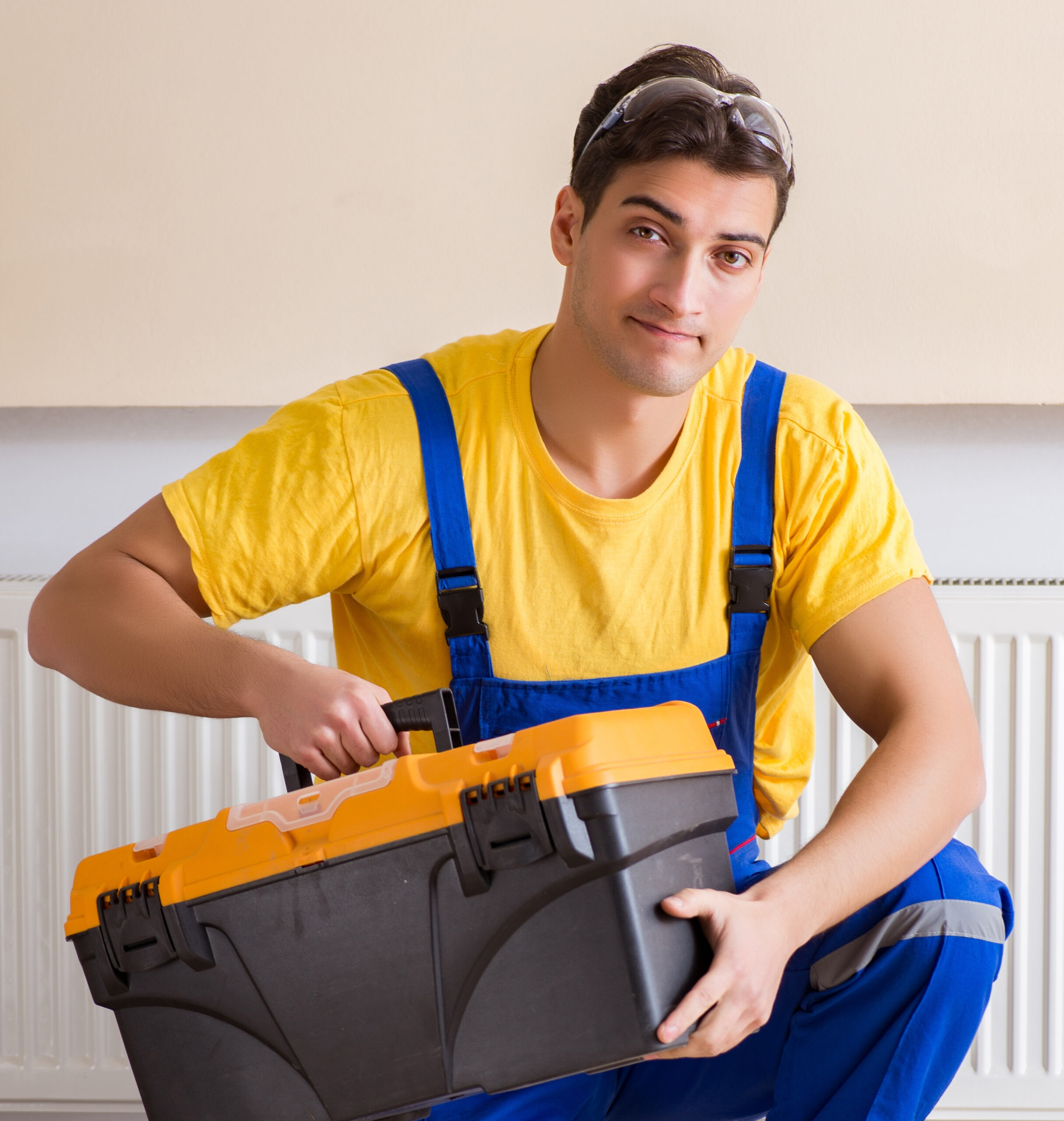 Technician in yellow shirt and blue overalls holding an orange and black toolbox.