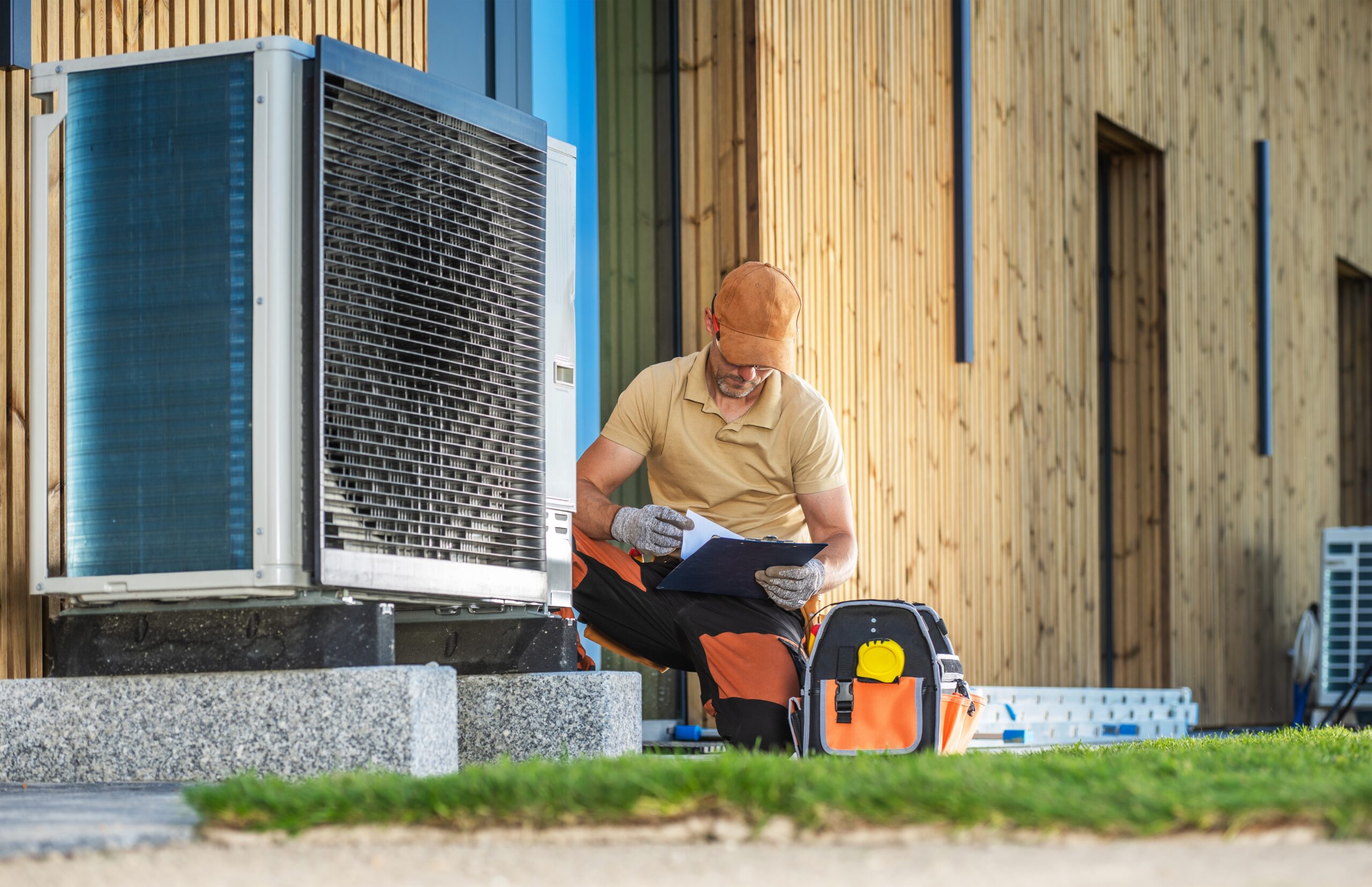 Technician in work gear reviewing documents next to an outdoor HVAC unit.